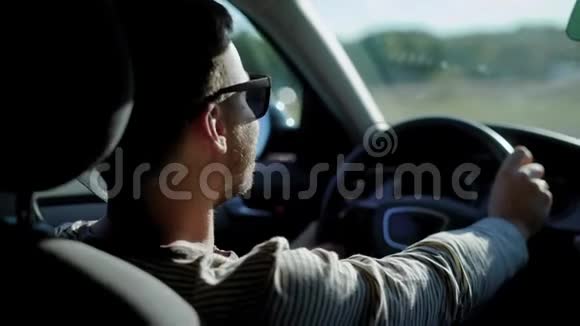 年轻英俊的男子独自坐在一辆车里在阳光明媚的日子里在高速公路上行驶看着后视镜视频的预览图