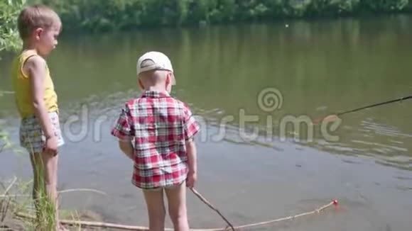 两个孩子站在河岸上在儿童棒的手中夏日炎炎视频的预览图