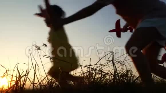 幸福的母女在美丽的夕阳背景下玩纸飞机的剪影视频的预览图