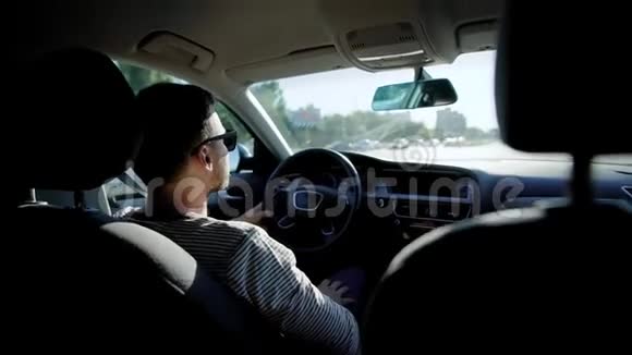 成年男子戴着太阳镜坐在车里开车在阳光明媚的夏日在城市街道上行驶视频的预览图