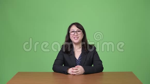 成熟漂亮的亚洲女商人坐在办公桌后一边对着镜头说话视频的预览图