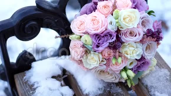 特写美丽的婚礼花束玫瑰乳制品白色和丁香花束躺在公园的雪凳上视频的预览图