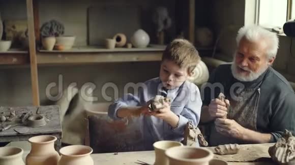 可爱的男孩在爷爷的陶艺工作室玩泥巴而老人在揉泥巴视频的预览图