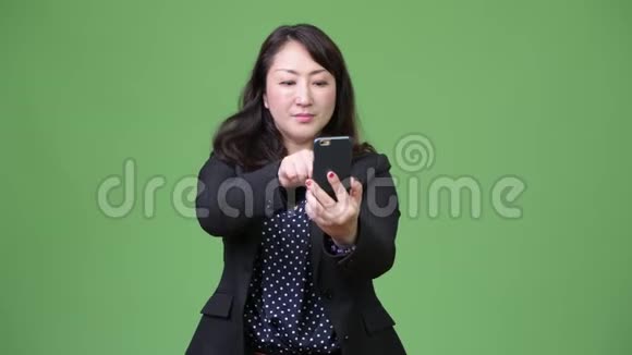 成熟美丽的亚洲女商人用电话和拇指视频的预览图