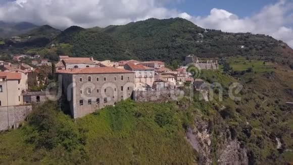 空中中世纪村庄在山上俯瞰海岸和山脉在有瓦屋顶的旧石楼上飞行视频的预览图