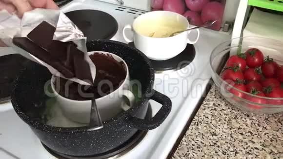 一个女人在一个容器里加入一块巧克力来融化它在炉子上的碗里放了一块黑白巧克力巧克力视频的预览图