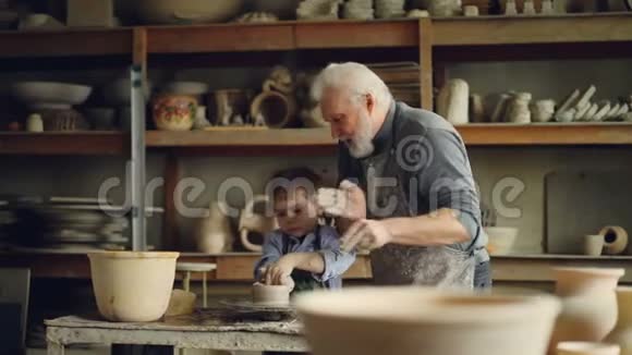 一位经验丰富的老人正在教小男孩如何在陶工车轮上使用粘土分享经验视频的预览图