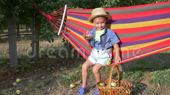 夏天口渴的孩子在果园果篮附近的吊床上喝着苹果鲜汁视频的预览图