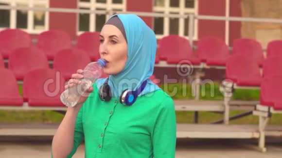 穆斯林运动女孩戴头巾坐着喝水的肖像视频的预览图