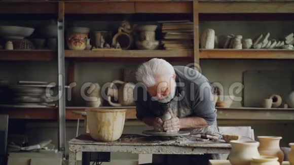 勤劳的白发男子正在陶工的车轮上用粘土加工塑造一块壤土精美的陶瓷器皿视频的预览图