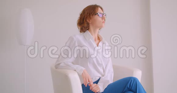 戴着眼镜的白种人成年女商人的特写肖像看着坐在扶手椅上的摄像机视频的预览图