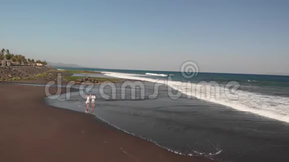 4K航空飞行视频的年轻夫妇使用无人机在海滩与黑色火山沙在日落时间巴厘岛视频的预览图