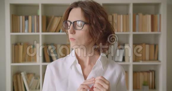 戴眼镜的白种人成年女商人用书架在室内看镜头的特写照片视频的预览图