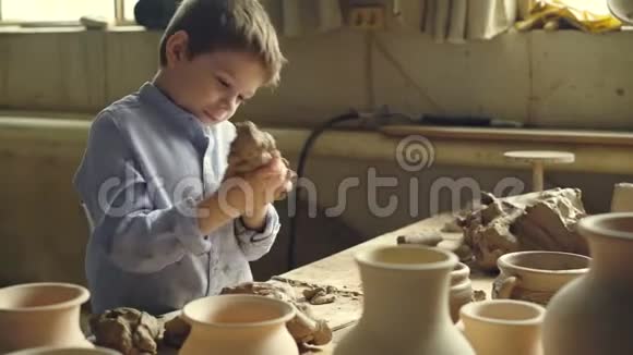 好奇的小男孩正在陶工车间的工作台上玩黏土捏黏土撕成碎片视频的预览图