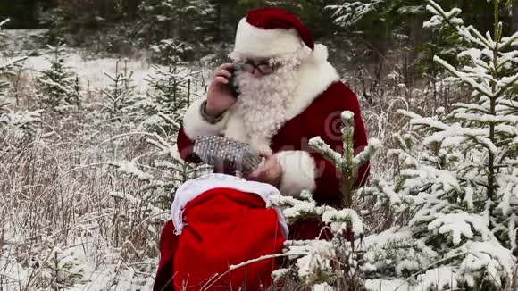 圣诞老人和智能手机在雪地森林的礼品袋附近视频的预览图