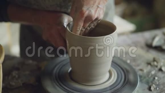 在家庭工作室用湿海绵在旋转壶的车轮上用男性手平滑成型粘土壶的特写镜头视频的预览图
