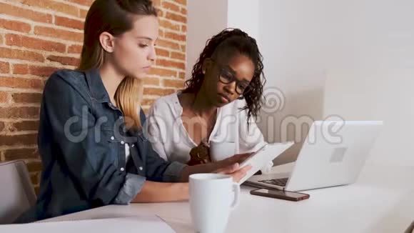 两个年轻漂亮的女商人在办公室里和数码平板电脑一起工作视频的预览图