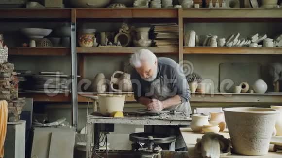 勤劳的银发男子正在陶工的车轮上用粘土加工塑造一块壤土精美的陶瓷器皿视频的预览图