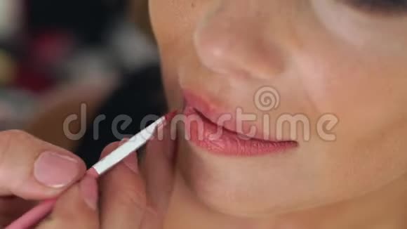 视觉师使用刷子在唇妆模型上应用口红关闭应用唇彩化妆师在做视频的预览图