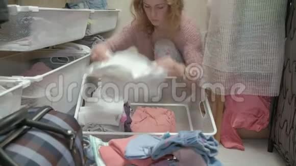 一个漂亮的女孩一个年轻的母亲在她的更衣室里捡起并把孩子们衣服叠在篮子里把东西放进去视频的预览图