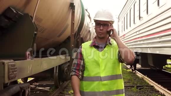 一个戴着眼镜戴着头盔穿着制服的工人在火车站边走边打电话的画像视频的预览图