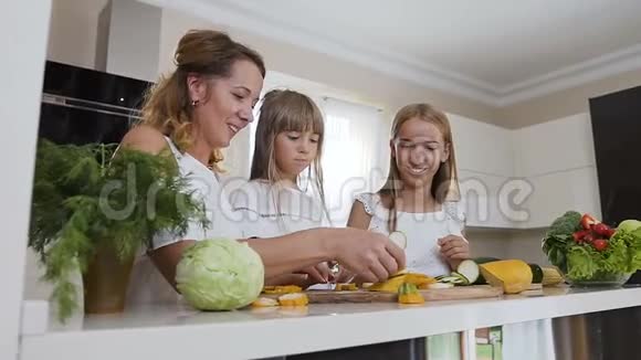 一位美丽的母亲带着两个穿着白色衣服的孩子在厨房的桌子上做了一个金字塔形的切碎的黄色西葫芦视频的预览图