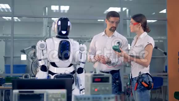 男性和女性工程师正在阅读带有特殊设备的类似人类的机器人视频的预览图