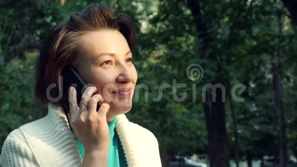 穿白色衬衫的女人坐在长凳上说着手机笑着看日落视频的预览图