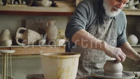 高级陶工正在陶瓷锅的底部工作在工作场所旋转陶工车轮创造传统视频的预览图
