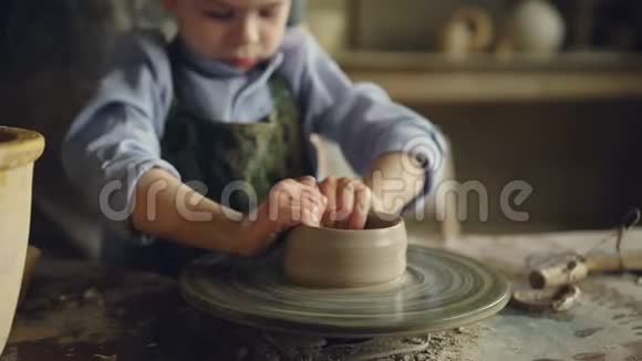 严肃的男孩在儿童中心上陶艺课时正在用粘土在投掷轮上花盆有意思视频的预览图