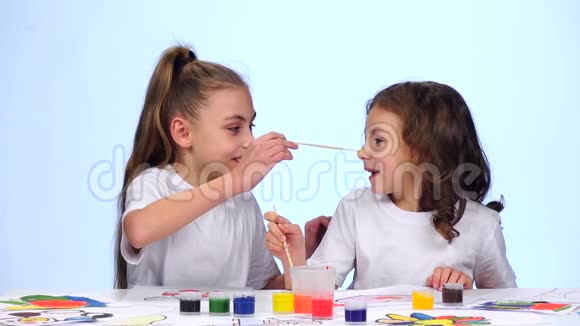 孩子们坐在桌子旁用画笔把自己涂在脸上白色背景慢动作视频的预览图