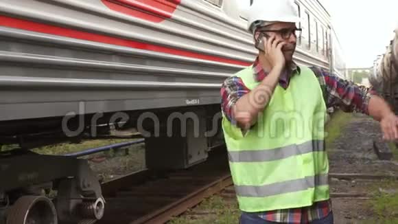 这个人是铁路公司的雇员穿着绿色夹克戴着火车背景上的头盔视频的预览图