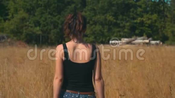 女孩慢慢地沿着金色的田野走向原木和针叶林视频的预览图