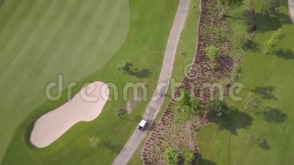 绿色高尔夫球杆和高尔夫球车在公路上行驶的美妙鸟眼全景视频的预览图