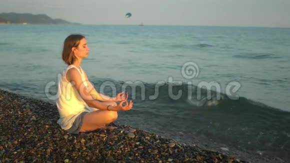 年轻女子在海滩上练习瑜伽和冥想日落视频的预览图