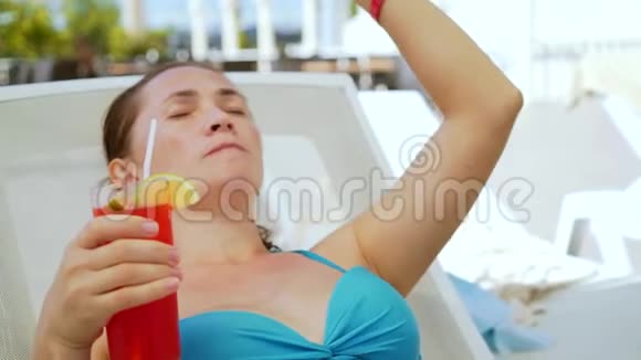 一个手里拿着鸡尾酒的女人坐在一个阳光休息室里戴墨镜的漂亮女孩在喝鸡尾酒视频的预览图