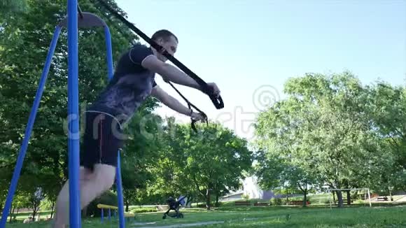 男人开始在一个夏季公园里的健身圈上做俯卧撑从下面的镜头4K慢镜头视频的预览图