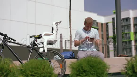 现代生活在一个大世界年轻人坐在城市的长凳上用智能手机重写视频的预览图