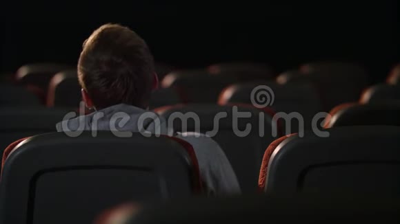 一个人坐在空荡荡的电影院大厅里年轻人在空荡荡的黑暗剧场里放松视频的预览图