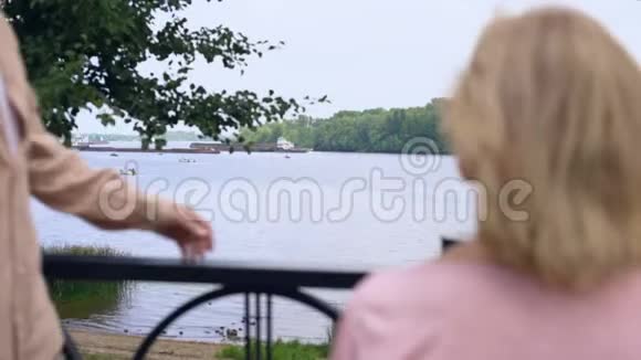 老人抱着女人在公园河边的花园里放松幸福的老年夫妇视频的预览图