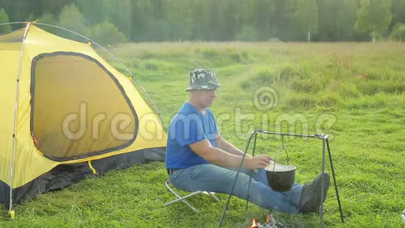 一个人靠近火边的帐篷看着一个沸腾的锅视频的预览图