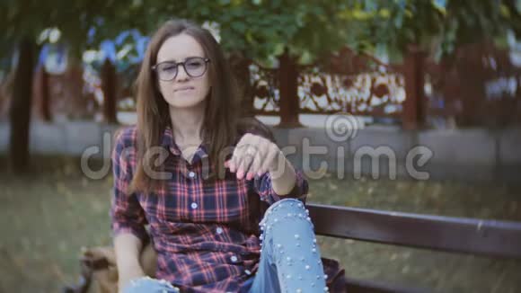 一位戴着眼镜坐在公园长椅上对着镜头微笑的可爱中年妇女视频的预览图