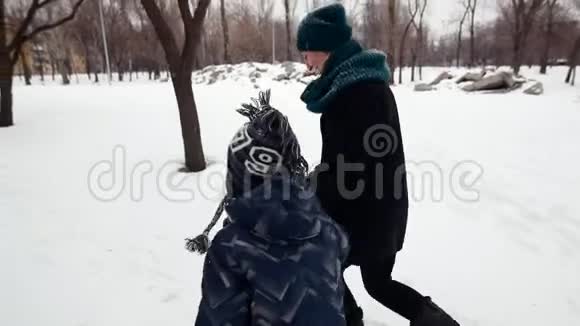 高清母子正快乐地在大雪覆盖的冬季公园里奔跑视频的预览图