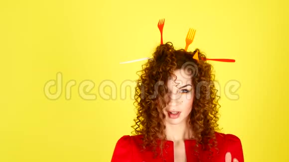 年轻漂亮的女人穿着黄色背景的红色连衣裙头发上有塑料叉子的女性肖像环境视频的预览图