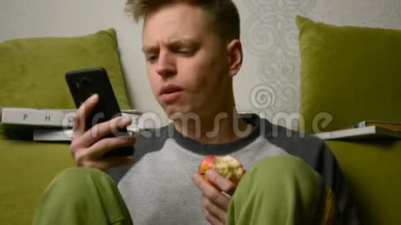 愤怒困惑和沮丧的年轻人看着手机吃东西视频的预览图