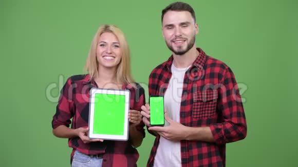 年轻夫妇一起展示数字平板电脑和智能手机视频的预览图