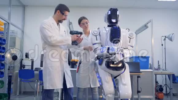 两名技术人员正在用钻头调整一个像人一样的机器人视频的预览图