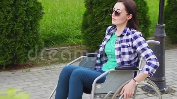 公园里坐在轮椅上穿着衬衫戴着眼镜的漂亮残疾女孩慢悠悠视频的预览图