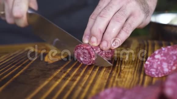 刀切香肠在木板上贴紧男性手拿刀切香肠腊肠餐桌视频的预览图
