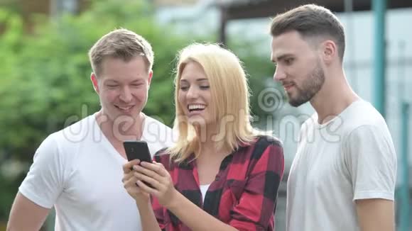三个快乐的年轻朋友在户外的街上一起用电话微笑视频的预览图